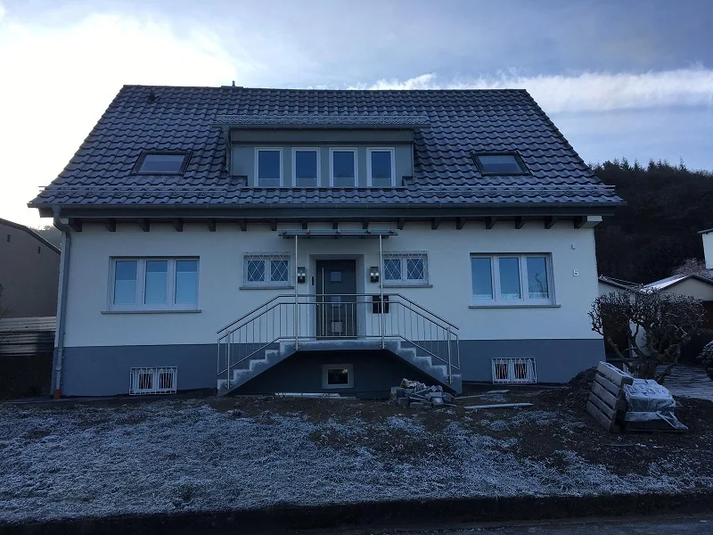 Helle Fassade eines Hauses mit dunklem Dach und Dachgaube