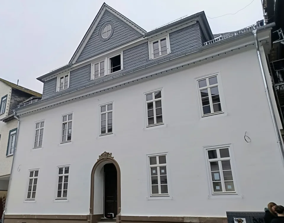 Fassade eines Wohnhauses mit hellem Putz und dunkler Dachgestaltung